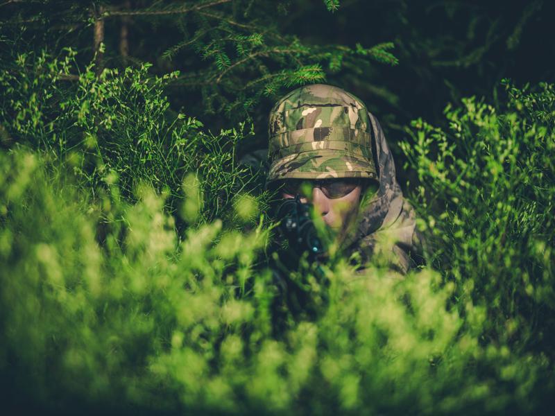 Camouflaged Poacher with Rifle at Hunt in the Dense Forest.