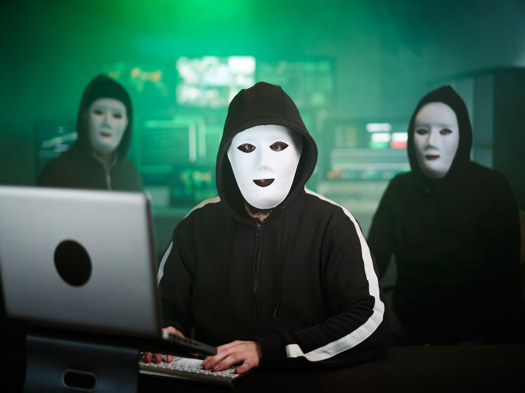 Masked Hacker is Using Computer for Organizing Massive Data Breach Attack on Corporate Servers. They’re in Underground Secret Location Surrounded by Displays